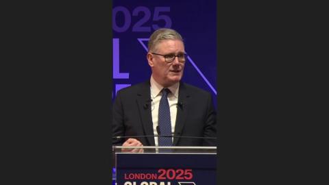 Keir Starmer, in a dark suit, speaks behind a podium