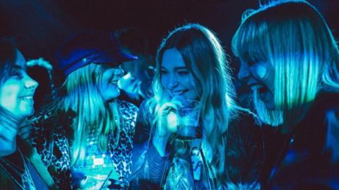 Four women with drinks in their hands, lit by a blue light