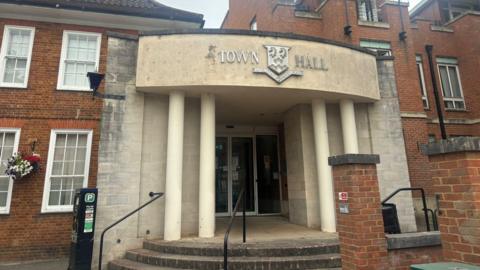 A building with steps and a large stone awning. A crest is on the awning with "town hall" written either side.