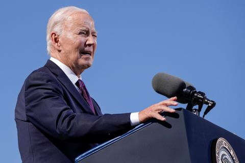 President Joe Biden speaking at a lectern, wearing sunglasses and a suit with a red tie