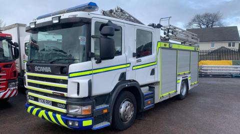 A parked white fire engine with fluorescent green stripes on it 