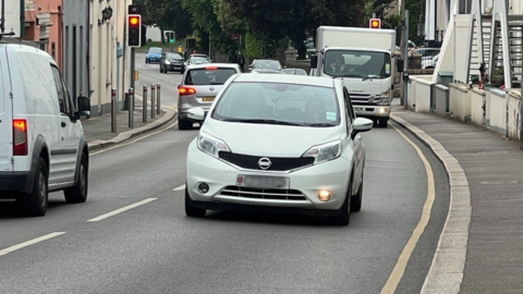 A wide shot of Rogue Bullion road. Driving towards the camera is a silver Nissan.