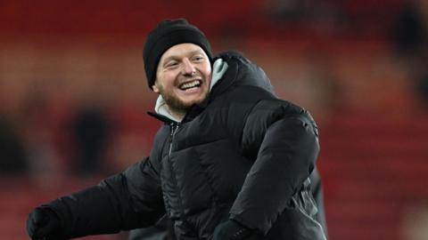 Kim Hellberg, wearing a woolly hat, thick padded coat and gloves, about to do a big fist pump towards the Middlesbrough fans
