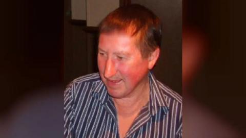 David Brickwood looking away from the camera lens in a dark but lit space. He is wearing a pinstriped navy blue and white shirt with the upper part of the shirt unbuttoned.