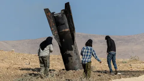Israeli settlers stand next to part of a missile protruding from the ground, following strikes from Iran, in the central Israeli-occupied West Bank, June 8, 2026.