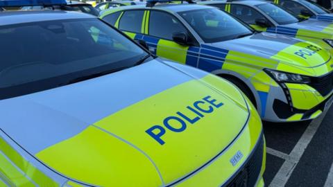 A close-up of a police car bonnet in line of marked police vehicles, parked in a row on a car park. 