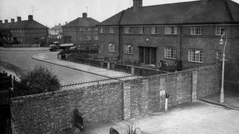A black and white archive image of the Cutteslowe Wall, seperating a privately developed housing estate and a council-built site