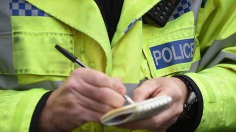 Stock image showing a close-up of a police officer writing on a notepad.