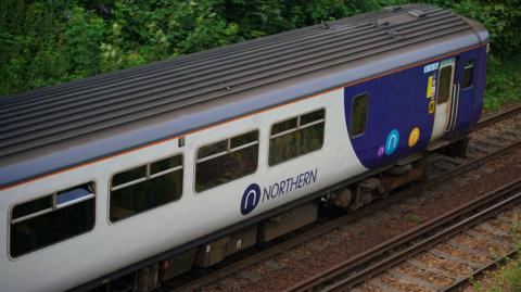 A grey and blue Northern train travelling on the rail tracks. 