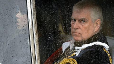 Andrew Mountbatten-Windsor seen through a carriage window - he is wearing ceremonial uniform. His daughter Eugenie can just be seen sitting alongside him