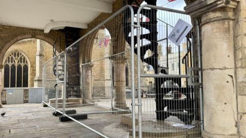 A metal fencing around a spiral black staircase inside the Guildhall with a bunting of the England flag in the background.