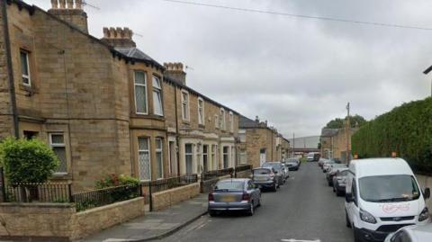A row of homes on a street with parked cars on either side of the road.