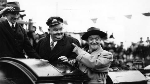A black and white picture of film stars Laurel and Hardy who are riding on a wagon.