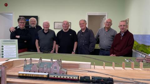 The group of volunteers who are making the model standing behind a miniature version of Axminster Station. 