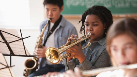 Three children playing brass instruments and looking at sheet music