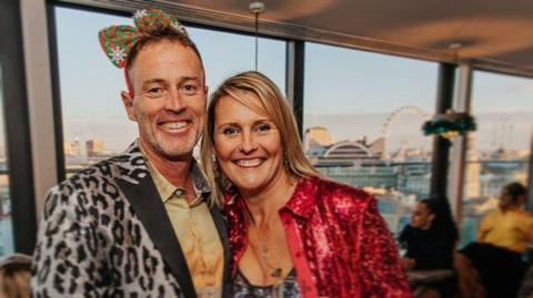 A middle-aged couple are in fancy dress at a party. They look happy.