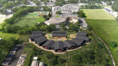 An aerial image of a school field with several black buildings in a semi-circle pattern