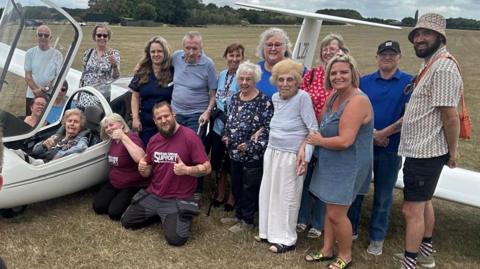 Mrs Gilliver sits in the cockpit, with friends, family and carers standing next to the plane 