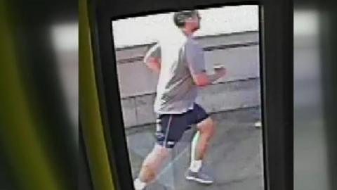CCTV still image from the inside of a bus showing a man in a grey T shirt and shorts running.
