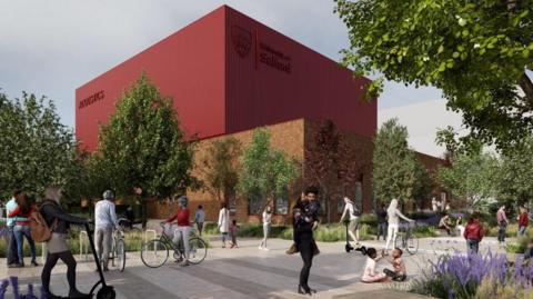 A CGI of a planned acoustics building in Salford. A large red metal building with the Salford University logo on stands in the background, with pedestrians and people on bikes walking on a pavement in the foreground 