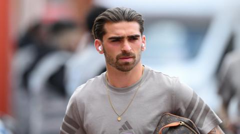 Jota Silva leaving a match at Forest wearing ear pods and a wash bag  