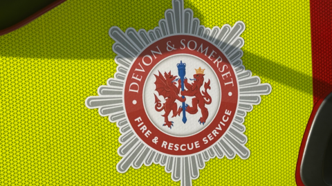 A picture of the logo for the fire service on the side of a vehicle. Its a silver and red logo. It is a green vehicle.