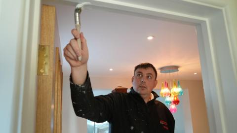 Picture of Norfolk bowler Wayne Willgress painting a door frame in a house. He is a decorator by trade when he is not playing bowls.