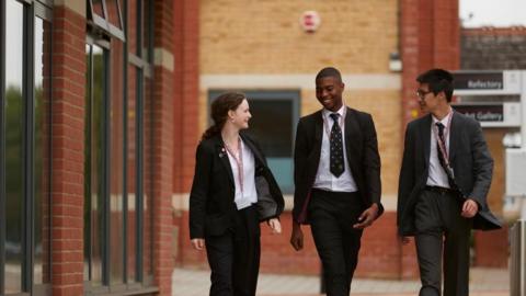 A stock photo from Pate's Grammar School showing three pupils in uniform walking alongside each other, with red-brick school buildings in the background
