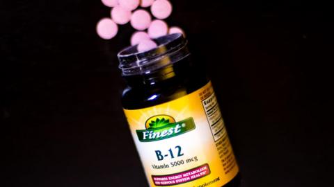 A bottle of vitamin B12 supplements. A handful of round-shaped pink tablets are shown near the rim of the bottle, which has a yellow label.