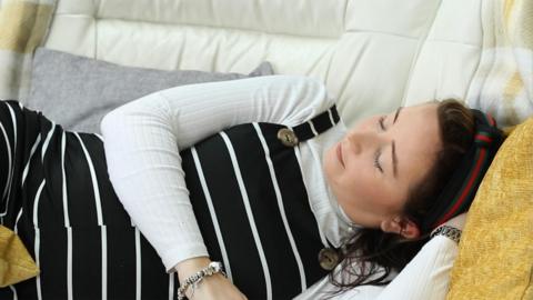 A pregnant mum in dungarees relaxes on the sofa.
