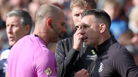 The referee speaks to Luton boss Matt Bloomfield