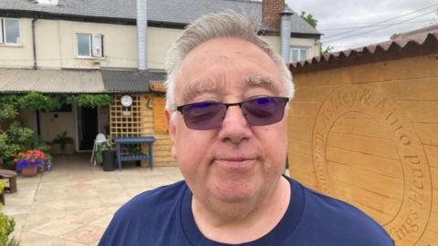 Paul English pictured outside his pub wearing sunglasses and a navy blue t-shirt. English has short shite hair and is clean shaven.