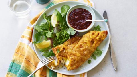 Battered fish on a plate alongside a mixed salad and relish