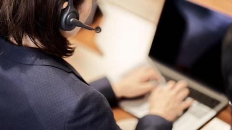 A person working on their laptop with a headset