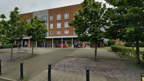 A convenient store, with trees and several benches in front of it.