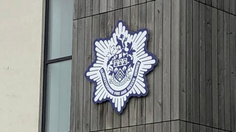 A blue and white logo showing the Gloucestershire Fire and Rescue Service crest on a building.