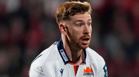 Ben Healy clutching the ball low down in both hands assessing his options in a match for Edinburgh