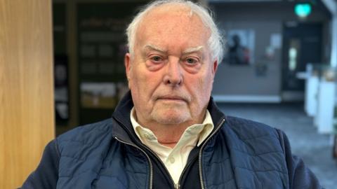 A man with white hair and a navy padded jacket 