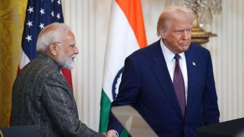India Prime Minister Narendra Modi shakes hands with President Donald Trump at the White House in February during a press conference. Behind the two men are the flags of India and the US. Modi stands in profile while Trump is looking forward.