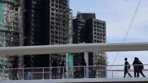 People walk on a foot bridge near the fire-ravaged Wang Fuk Court housing complex