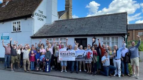 About 30 people on the pavement outside The Ickleton Lion pub holding a banner