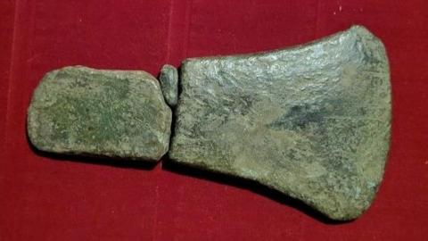 Three pieces of an old axe head, sitting in a box with a red base, after their discovery.