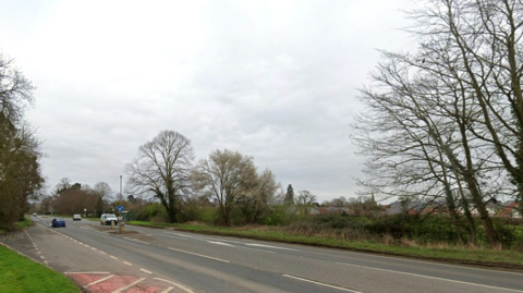 The view across the A49 to the field which can now be developed for housing. Trees line the boundary of the field by the main road.