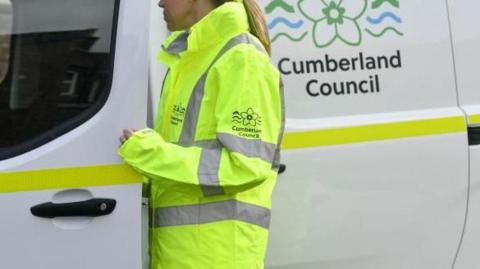 A Cumberland Council worker in a branded high-visibility jacket getting into a white, branded van.