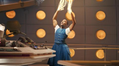 Ncuti Gatwa as the Doctor regenerating. He is holding his hands up in the air and looking at them as light comes out from them and shooting upwards.
