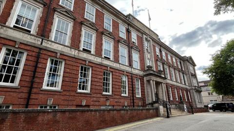 Lincolnshire County Hall a three-storey red brick building with grey stone pillars and steps with black bannisters at the main entrance 