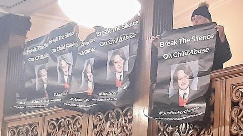 Protesters on a balcony at the town hall holding black banners which say Break the Silence on Child Abuse with the picture of a schoolgirl underneath