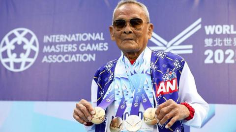 Sawang Janpram wears sunglasses as he shows off the four gold medals hanging around his neck
