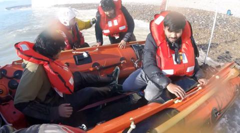 Two men in lifejackets on an inflatable lifeboat at sea with a couple of RNLI rescuers also in the boat