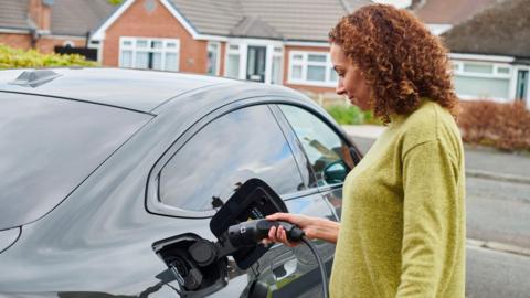 Woman charging an electric car parked on her drive